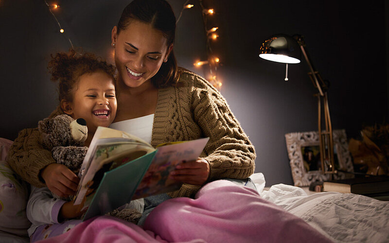 Eine Frau liest ihrem Kind ein Buch vor dem Einschlafen vor.