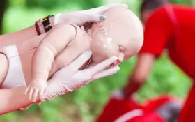 Erste Hilfe Kurs mit einer Säuglingspuppe, die mit dem Gesicht nach unten auf einem ausgestreckten Arm liegt.