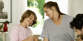 Eine Familie, bestehend aus Vater, Mutter und Kind, sitzen am Esstisch und spielen Spiele.