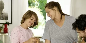 Eine Familie, bestehend aus Vater, Mutter und Kind, sitzen am Esstisch und spielen Spiele.