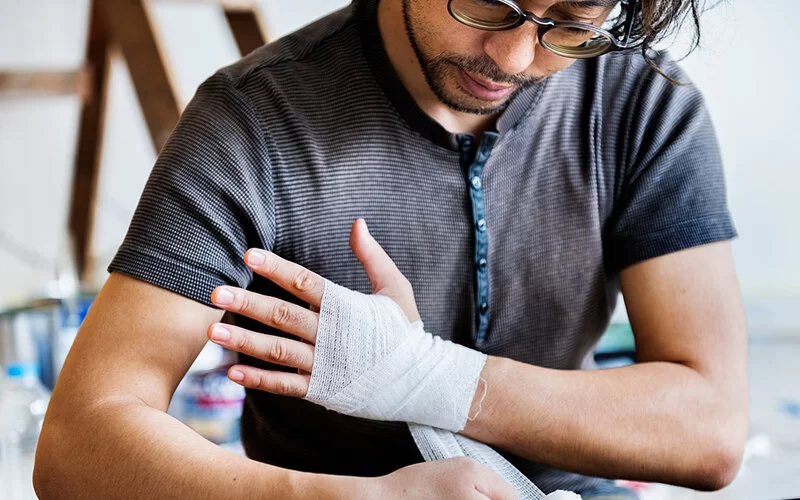Ein Mann mit Verbrennungen an der Hand versorgt sich selbst mit sterilem Verband.