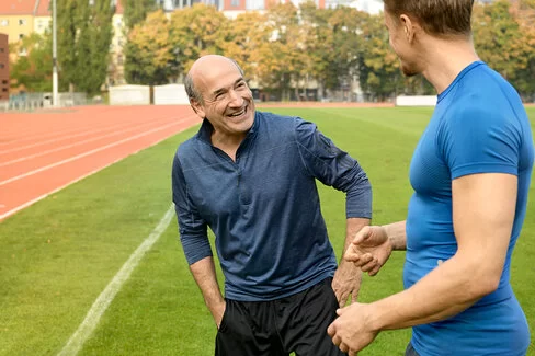 Ein älterer und ein jüngerer Mann bereiten sich auf einem Sportplatz auf ein Rückentraining vor..