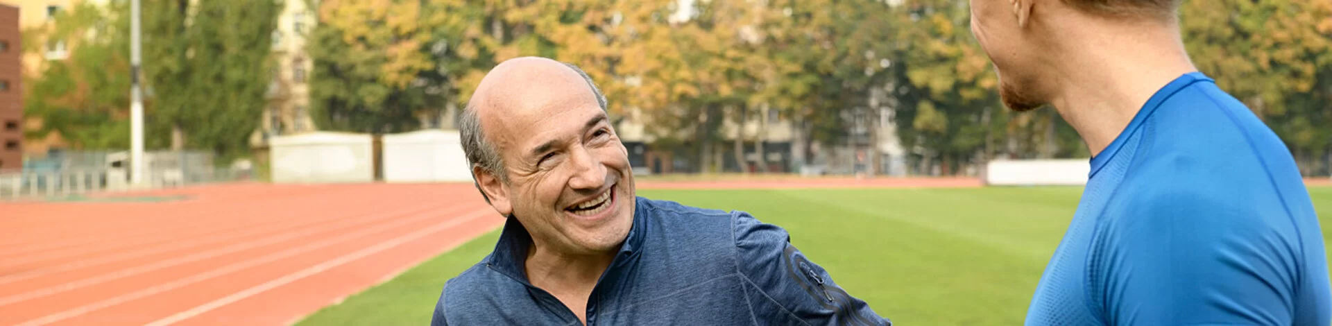 Ein älterer und ein jüngerer Mann bereiten sich auf einem Sportplatz auf ein Rückentraining vor..