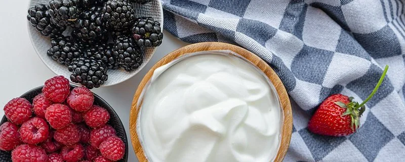 Eine Schale mit Joghurt steht neben zwei Schalen mit frischen Beeren.
