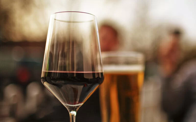 Ein Rotweinglas steht im Vordergrund, im Hintergrund ein Glas Bier. 