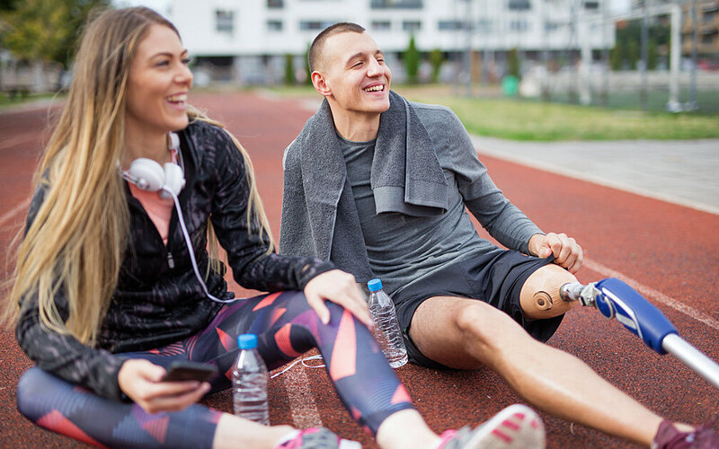 Junger Mann mit Beinprothese ruht sich gemeinsam mit einer Freundin nach dem Sport aus.