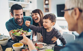 Eine Familie mit Kind isst gemeinsam an einem Tisch, sie ernähren sich gesund und abwechslungsreich.