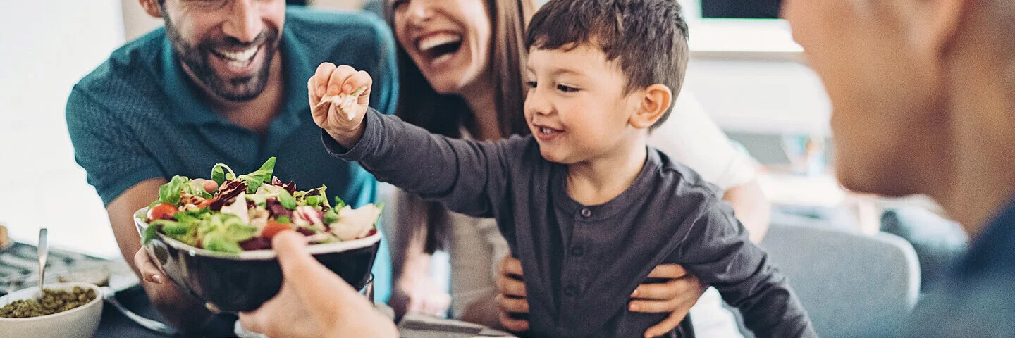 Eine Familie mit Kind isst gemeinsam an einem Tisch, sie ernähren sich gesund und abwechslungsreich.