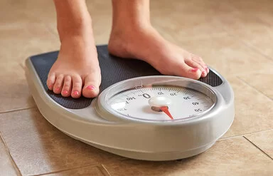 Weibliche Füße auf einer analogen Personenwaage mit runder Anzeige.
