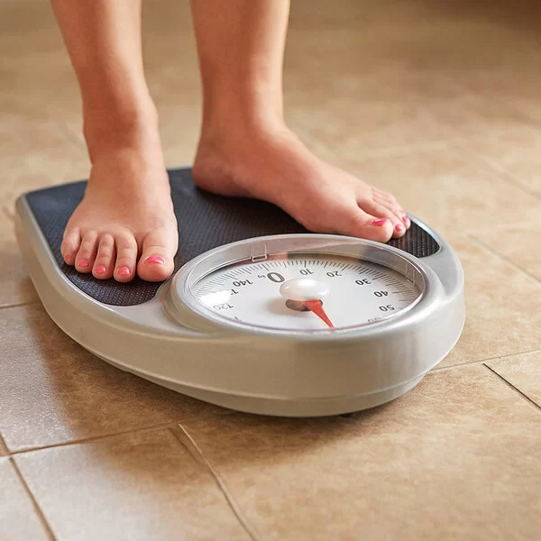 Weibliche Füße auf einer analogen Personenwaage mit runder Anzeige.