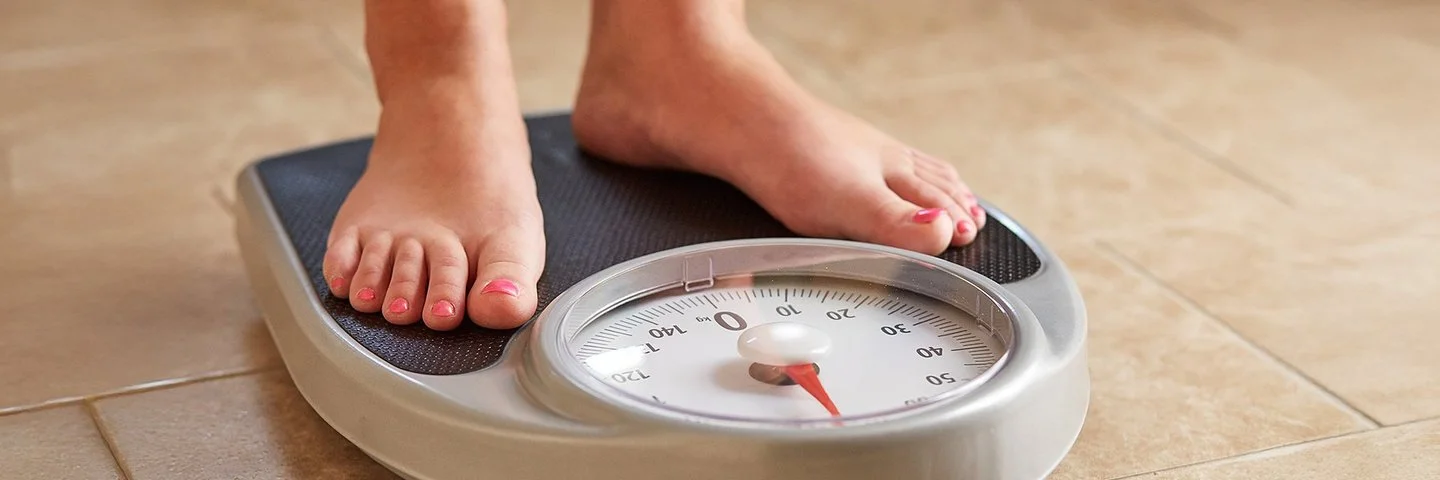 Weibliche Füße auf einer analogen Personenwaage mit runder Anzeige.