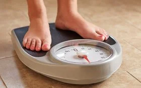 Weibliche Füße auf einer analogen Personenwaage mit runder Anzeige.