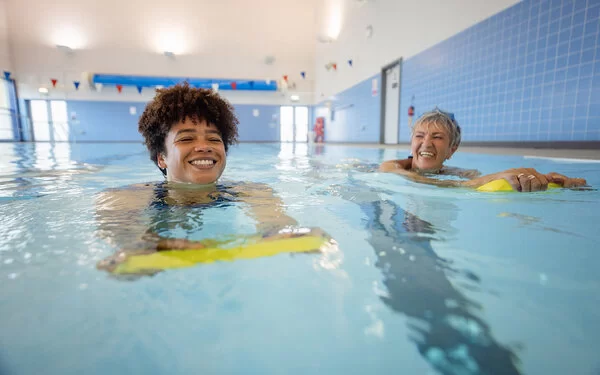 Zwei erwachsene Frauen mit Schwimmhilfe im Wasserbecken lernen Schwimmen.