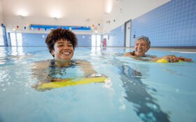 Zwei erwachsene Frauen mit Schwimmhilfe im Wasserbecken lernen Schwimmen.