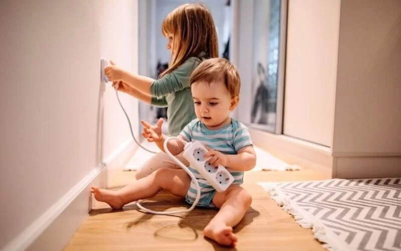 Zwei kleine Kinder spielen mit Steckdosen herum. 