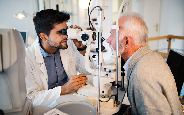 Ein junger Augenarzt führt eine Augenuntersuchung mit einem Spaltlampengerät bei einem älteren Mann durch.