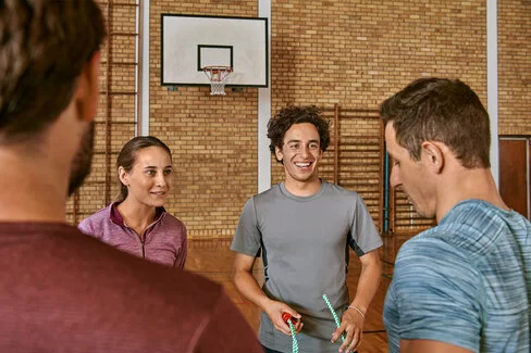 Eine fröhliche Gruppe mittleren Alters bei einem Bewegungskurs in einer Sporthalle.