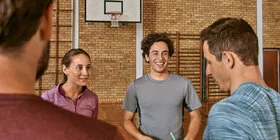 Eine fröhliche Gruppe mittleren Alters bei einem Bewegungskurs in einer Sporthalle.