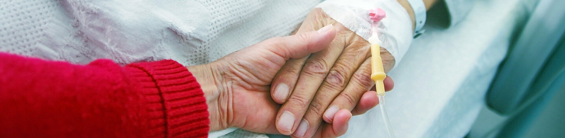 Eine Frau hält die Hand eines Patienten im Krankenhaus. Stirbt der Patient, führen Ärzte vor der Organspende eine Hirntoddiagnostik durch.