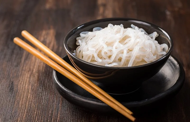 Eine Schüssel mit zubereiteten Konjaknudeln, daneben liegen zwei Essstäbchen.