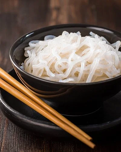 Eine Schüssel mit zubereiteten Konjaknudeln, daneben liegen zwei Essstäbchen.