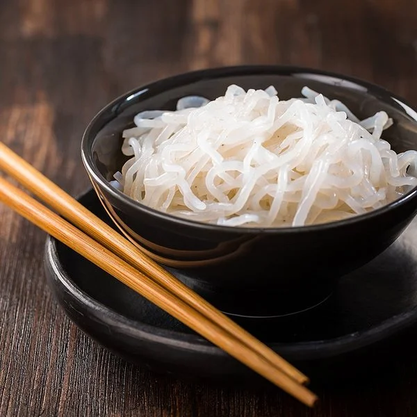 Eine Schüssel mit zubereiteten Konjaknudeln, daneben liegen zwei Essstäbchen.