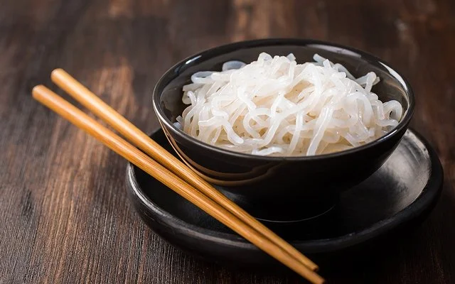 Eine Schüssel mit zubereiteten Konjaknudeln, daneben liegen zwei Essstäbchen.