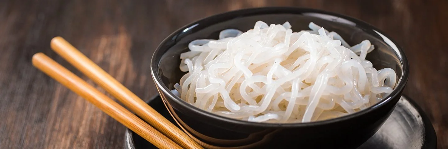 Eine Schüssel mit zubereiteten Konjaknudeln, daneben liegen zwei Essstäbchen.