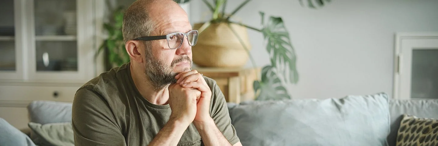 Ein Mann sitzt auf einer Couch und schaut nachdenklich zur Siete.