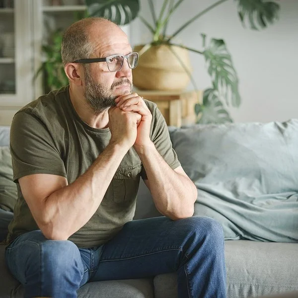 Ein Mann sitzt auf einer Couch und schaut nachdenklich zur Siete.