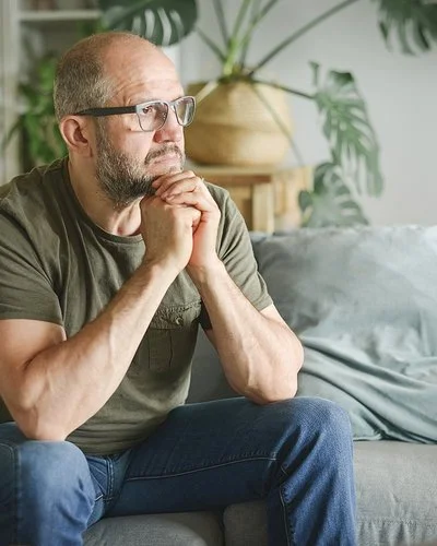 Ein Mann sitzt auf einer Couch und schaut nachdenklich zur Siete.