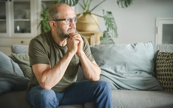 Ein Mann sitzt auf einer Couch und schaut nachdenklich zur Siete.