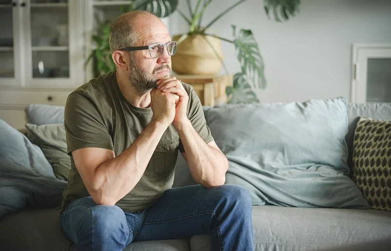 Ein Mann sitzt auf einer Couch und schaut nachdenklich zur Siete.