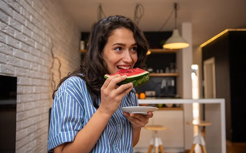 Eine junge Frau beißt genüsslich in eine Scheibe Wassermelone.