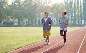 Eine Frau und ein Mann joggen auf einem Sportplatz.