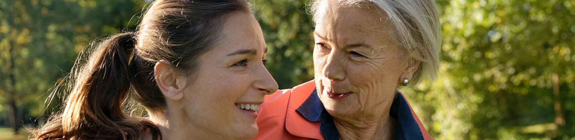 Zwei Frauen machen lachend und Arm in Arm einen Spaziergang durchs Grüne.