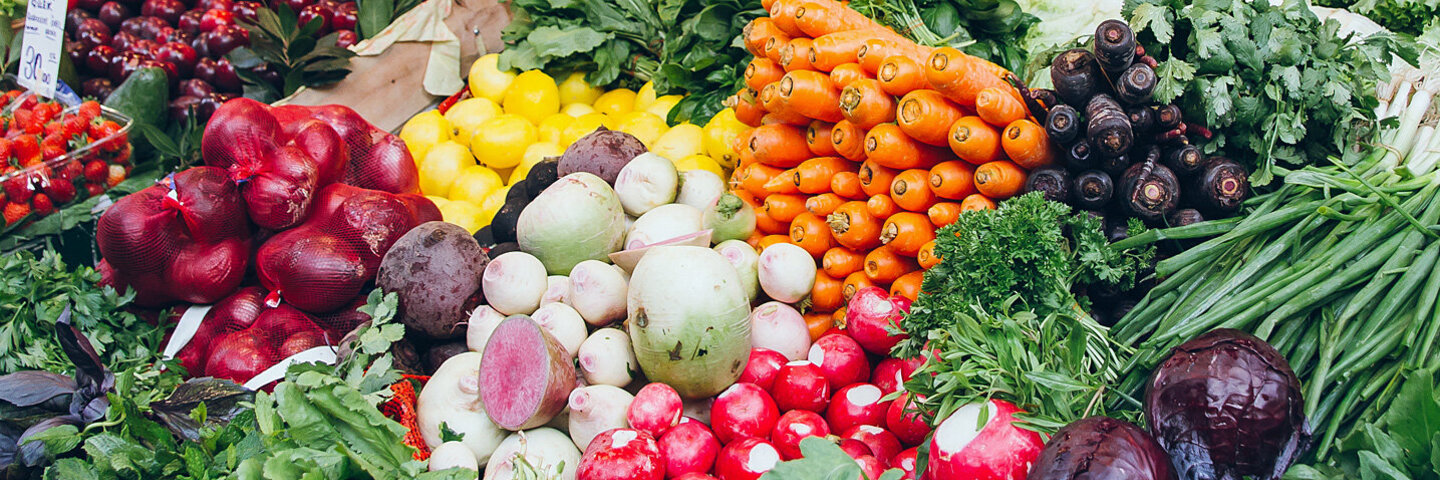 Obst und Gemüse liegen üppig präsentiert auf einem Marktstand.