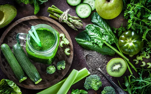 Ein frischer grüner Smoothie im Glas, umgeben von frischem Gemüse wie Zucchini, Spinat und Paprika.