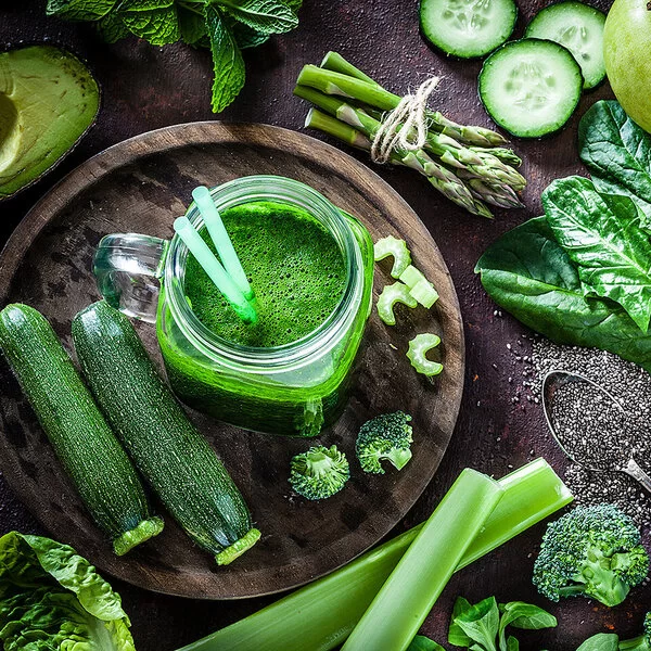Ein frischer grüner Smoothie im Glas, umgeben von frischem Gemüse wie Zucchini, Spinat und Paprika.