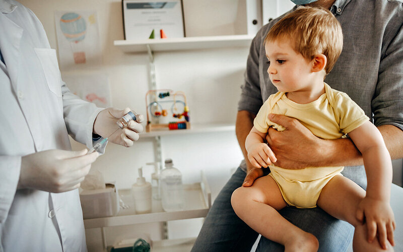 Kind schaut beim Arzt auf Spritze. Es wird geimpft, weil der Nestschutz nicht mehr besteht.