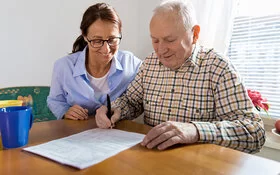 Eine ambulante Pflegekraft hilft einem älteren Mann beim Ausfüllen eines Antrags.