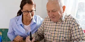 Eine ambulante Pflegekraft hilft einem älteren Mann beim Ausfüllen eines Antrags.