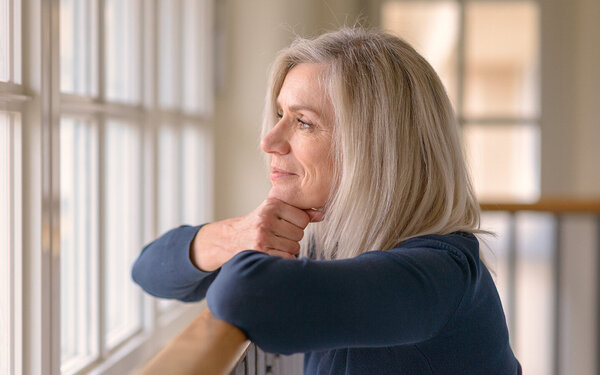 Eine blonde Frau schaut nachdenklich aus dem Fenster und grübelt über ihre Selbstliebe.