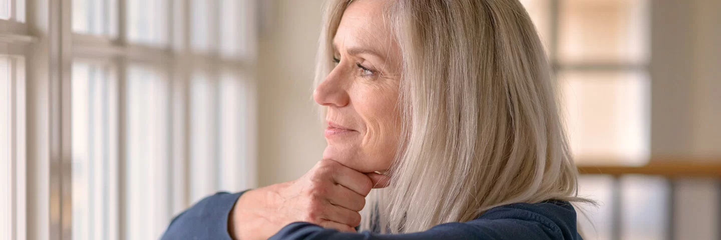 Eine blonde Frau schaut nachdenklich aus dem Fenster und grübelt über ihre Selbstliebe.