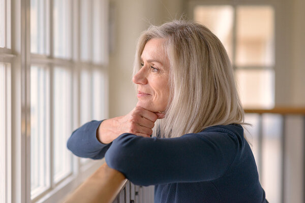 Eine blonde Frau schaut nachdenklich aus dem Fenster und grübelt über ihre Selbstliebe.