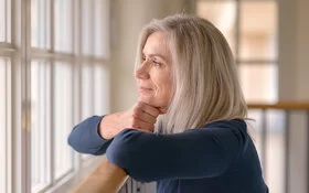 Eine blonde Frau schaut nachdenklich aus dem Fenster und grübelt über ihre Selbstliebe.