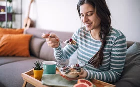 Eine Frau isst Joghurt mit Müsli und Beeren, um ihre Verdauung anregen.