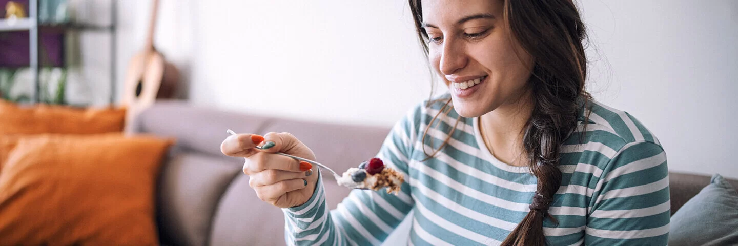 Eine Frau isst Joghurt mit Müsli und Beeren, um ihre Verdauung anregen.