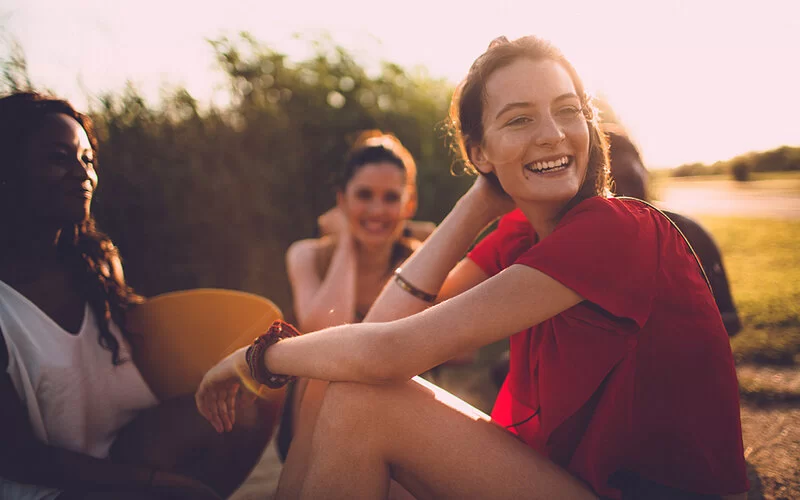 Junge Leute sitzen im Park in der Sonne zusammen und lachen.