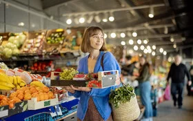 Eine junge Frau kauft Obst und Gemüse in einer Markthalle.